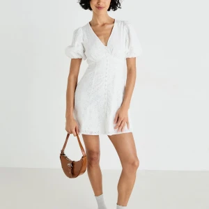 Vit kort klänning från gina - Superfin vit kort klänning i bomull med broderade blommor, puffärmar och v-ringning. Snygga klädda knappar framtill och lätt a-linjeformad passform. Perfekt för sommarens alla tillfällen! 