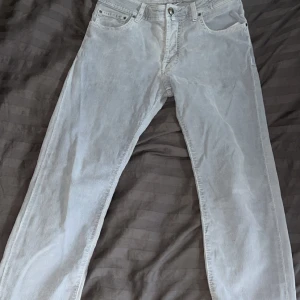 Ljusgrå manchesterbyxor Jacob Cohen - Snygga ljusgrå manchesterbyxor från Jacob Cohen med klassisk femficksdesign och raka ben. Byxorna har diskret logga på myntfickan och mörkblå patch bak i midjan. Perfekta för dig som gillar stilrena och bekväma byxor i mjukt material. De ser ut som jeans från långt avstånd men har ett skönt manchestermaterial som erbjuder komfort och stil!