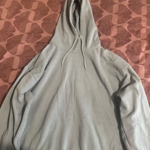 Ljusgrön hoodie från Lager 157, storlek M - En stilren ljusgrön hoodie från Lager 157 i storlek M. Tröjan har huva med snörning och är tillverkad i mjukt material som känns skönt mot huden. Perfekt för chill dagar eller när du vill ha en enkel och clean look.
