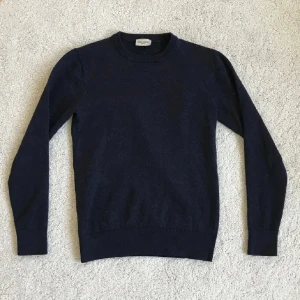 Mörkblå merinoullströja John Henric - Klassisk mörkblå rundhalsad tröja från John Henric i 100% mjuk merinoull. Enkel och stilren design med ribbade muddar vid ärmslut och nederkant. Perfekt för lager-på-lager och passar till allt. Står S i tröjan men den passar Xxs-xs 