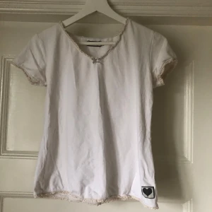 Vit topp med spets - Supersöt vit topp med v-ringning, liten rosett framtill och spetsdetaljer längs kanterna🩷🐩