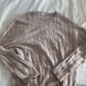 Beige stickad tröja J.Lindeberg S - Säljer en beige stickad tröja från J.Lindeberg i storlek S. Tröjan har ett snyggt strukturmönster med diamantformade rutor, rund halsringning och ribbade muddar vid ärmslut och nederkant. Perfekt för dig som gillar stilrena och bekväma plagg.