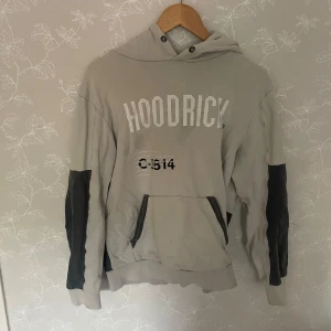 Beige och svart hoodie från Hoodrick - Snygg beige hoodie från Hoodrick med svart tryck och detaljer. Stor HOODRICK-text framtill, coolt världskarta-tryck på ryggen och svarta partier på ärmar och nedtill. Känguruficka och huva gör den extra chill. Perfekt för dig som gillar streetwear.