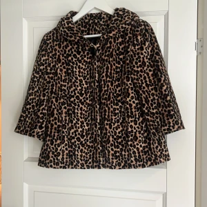 Leopardmönstrad pälsjacka med huva - Säljer en fluffig pälsjacka med leopardmönster och trekvartsarmar. Jackan har vida ärmar och är i en beige och brun färgskala med svarta detaljer. Perfekt för dig som vill sticka ut och hålla dig varm under kyliga dagar.