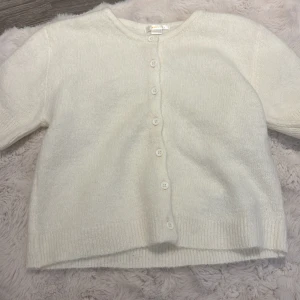 Vit tröja från Gina Tricot - Mysig vit tröjafrån Gina Tricot i storlek 158/164. Tröjan är stickad, har rund halsringning och stängs med vita knappar framtill. Perfekt för lager-på-lager och enkel att matcha med olika outfits.