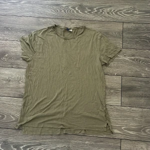 Olivgrön basic t-shirt - Enkel olivgrön t-shirt med rund hals och korta ärmar. Modellen är rak och lite längre i passformen, med små slitsar i sidorna. Perfekt för en avslappnad och chill stil. T-shirten är tillverkad i mjukt material som känns skönt mot huden.
