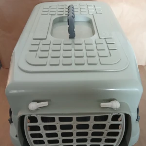 Hundtransportbur - Bilderna visar en grå transportbur för husdjur, t.ex. katt eller liten hund. Buren har ett robust handtag, ventilationshål på sidorna och ett galler i plast framtill. Perfekt för dig som vill resa säkert med ditt djur. Märkt med Biltema på undersidan.                           Kan skickas med extra pris via post.               