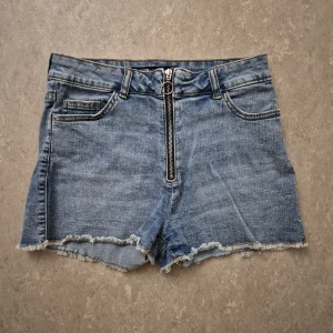 Jeansshorts - Snygga ljusblå högmidjade jeansshorts från FB Sister med råa kanter och dragkedja framtill. Klassisk femficksmodell och bälteshällor. Perfekta för varma sommardagar och enkel att matcha med allt.