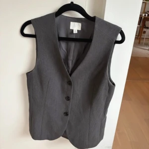 Grå väst från H&M -  grå väst från H&M i klassisk passform med tre knappar framtill och v-ringad hals. Knappt använt i jättefint skick 😍