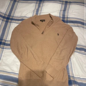 Beige stickad half zip från Polo Ralph Lauren - Säljer en beige stickad tröja från Polo Ralph Lauren med half zip och broderad logga på bröstet. Tröjan har lång ärm, ribbade muddar och klassisk krage. Perfekt för dig som gillar stilren och tidlös design. Skicka ett pm för fler frågor