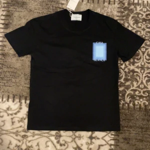 Svart t-shirt Casablanca Tennis Club - Svart t-shirt från Casablanca Tennis Club med blått grafiskt tryck och texten 'Casa Blanca' på bröstet och ryggen. Klassisk passform och rund hals. Perfekt för dig som gillar stilrena statement-plagg.