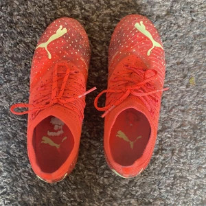 Röda Puma fotbollsskor med snörning - Säljer ett par röda Puma fotbollsskor med gula detaljer och snörning. Skorna har stickad ovandel med små vita prickar och en gul sula med dobbar för bra grepp på planen. Perfekta för dig som vill sticka ut på fotbollen!