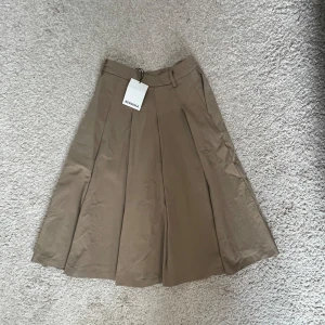 Beige långkjol från Bershka XS - Snygg beige långkjol från Bershka i storlek XS. Kjolen har bred linning med hällor, djupa veck framtill och en klassisk A-linjeformad siluett. Perfekt för dig som gillar stilrena och tidlösa plagg med en modern twist.