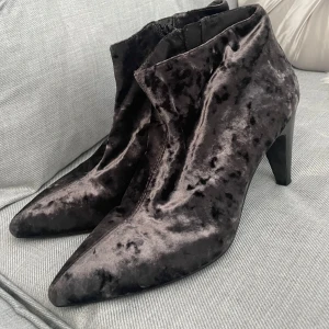 Svarta sammetsstövletter med klack - Snygga svarta stövletter från Vagabond i glansig sammetslook. De har spetsig tå, hög klack och dragkedja på insidan. Perfekta för dig som vill sticka ut med ett par unika boots i mjukt material och cool finish. 