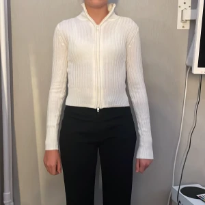 Vit ribbad kofta från H&M XS - Säljer en vit ribbad kofta från H&M i storlek XS. Tröjan har lång ärm, hög krage och hel dragkedja framtill. Den är stickad i ett mjukt material och har en slim passform som sitter snyggt på kroppen. Perfekt till lager-på-lager och enkel att matcha.