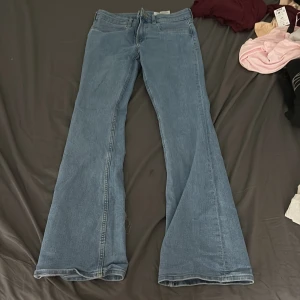 Blå bootcut jeans från H&M - Snygga ljusblå bootcut jeans från H&M med låg midja. Jeansen har klassisk femficksdesign och är tillverkade i bomull med en skön jeanskänsla. Perfekta för dig som gillar retrovibbar och vill ha ett par jeans med utsvängda ben.