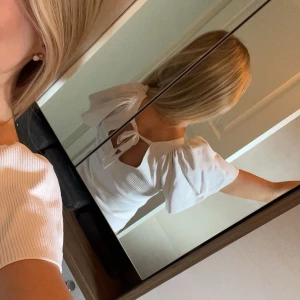 Vit ribbad topp med knyt i ryggen - Supersöt vit ribbad topp med korta puffärmar och v-ringning. Toppen har en snygg öppen rygg med knytband som detalj. Perfekt till jeans eller kjol för en fräsch och trendig look. Materialet känns mjukt och följsamt. Osäker på varumärket då jag klippt av lappen men gissar att den är från vila eller liknade..