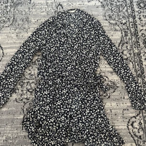 Blommig omlottklänning från ONLY - Supersöt kort omlottklänning från ONLY i navy blue med vitt blommönster. Klänningen har långa ärmar, volangdetaljer och knyt i midjan. Perfekt för dig som gillar en feminin och trendig stil med v-ringad hals och skön passform.