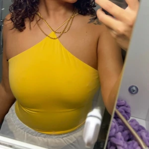 Gul halterneck tubtopp - Snygg gul tubtopp med halterneck och smala axelband som korsas i nacken. Toppen är tight och croppad, perfekt för att sticka ut. Mjuk och stretchig känsla, passar till många olika stilar.