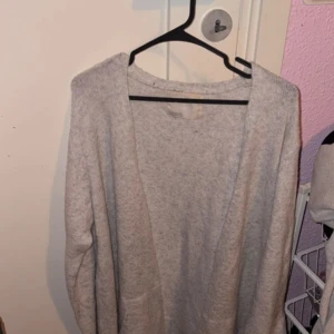 Ljusgrå stickad kofta med fickor - Mysig ljusgrå stickad kofta från Cubus med långa ärmar och öppet framtill. Koftan har två praktiska fickor och en enkel, clean design som är lätt att matcha med olika outfits. Perfekt för kyliga dagar när du vill ha något bekvämt och stilrent.