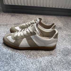 Maison Margiela sneakers  - Maison Margiela sneakers med klassisk design i skinn och mocka. Snygga paneler, rund tå och platt gummisula i brunt. Skorna har snörning och en stilren look som passar till jeans eller dressade outfits. Perfekt för dig som gillar minimalistisk stil och premiumkänsla.