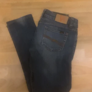 Blå jeans från Nudie Jeans - ! Dålig kamera ! Säljer ett par klassiska blå jeans från Nudie Jeans med snygga slitningar och kontrastsömmar. Jeansen har fem fickor, normal passform och är tillverkade i slitstarkt denim. Perfekta för dig som gillar en tidlös och stilren look.