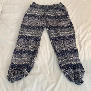 Mönstrade blåvita linnebyxor/yoga - Säljer ett par chill blåvita linnebyxor med snyggt etniskt mönster. Byxorna har resår i midjan och snörning för extra komfort. Materialet är lätt och luftigt, perfekt för varma dagar. Passformen är loose och benen är lite croppade med resår vid benslut.