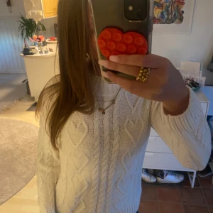 Vit stickad tröja med hjärtmönster H&M - Supermysig vit stickad tröja från H&M med högt ribbat halslinning och snygga flätade detaljer samt hjärtmönster på framsidan. Perfekt för kyliga dagar och passar till jeans eller kjol. Långärmad och med ribbade muddar för extra komfort.