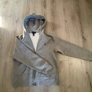 Grå hoodie från Ralph Lauren - Säljer en stilren grå hoodie från Ralph Lauren med dragkedja och klassisk logga på bröstet, säljer vidare då den inte passar mig, hör av en vid frågor. Pris kan diskuteras!