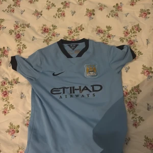 Manchester City blå fotbollströja Nike - Snygg Manchester City fotbollströja med klassisk ljusblå färg och svarta detaljer 147-158 cm stor och 13-14 år 