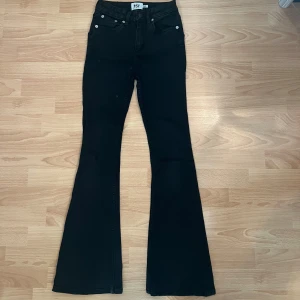 Svarta flare jeans från 157+ gul tubtopp, XS - Svarta jeans från 157 i modellen Snake Flare, storlek XS short lenght. Snyggt utsvängda ben med klassisk femficksdesign och knappstängning. Jeansen har en stilren look och är gjorda i mjukt denimtyg med stretch för extra komfort. En egensydd söt gul tubtopp medföljer även!
