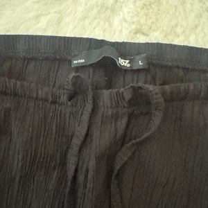 Svarta linnebyxor från 157 L - Säljer ett par svarta linnebyxor från 157 i storlek L. Byxorna har en avslappnad passform med resår och snörning i midjan. Materialet är lätt och har en snygg skrynklig struktur som ger en chill vibe. Perfekta för varma dagar eller när du vill vara extra bekväm.