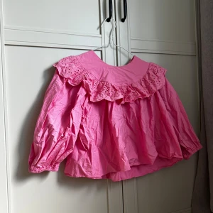 Rosa volangblus från Zara - Supersöt rosa blus från Zara med bred krage och broderad volangdetalj runt axlarna. Blusen har puffiga långärmar med resår vid ärmslut och knäppning bak i nacken.🌸🩷