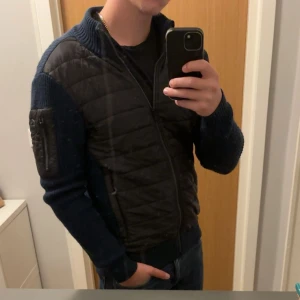 Mörkblå hybridjacka från Snoot - Säljer en snygg mörkblå hybridjacka från Snoot. Jackan har quiltad front i syntetmaterial och stickade ärmar och rygg. Dragkedja framtill och praktisk ficka med dragkedja på ena ärmen. Nypris runt 2000 kr. Inte skråmor och inte alls mycket använt. Vid frågor är det bara att skriva! Den är i mycket bra skick.