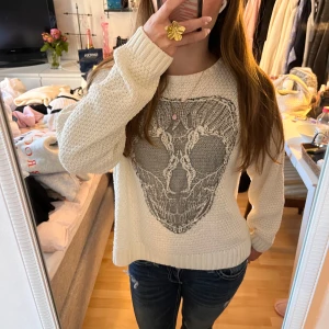 stickad tröja från Gina Tricot - Säljer en vit stickad tröja från Gina Tricot i storlek XS. Tröjan har ett stort grått döskallemotiv framtill och är långärmad med ribbade muddar vid ärmslut och nederkant. Perfekt för dig som gillar edgy detaljer och vill sticka ut.