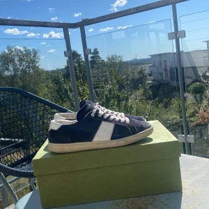 Saint Laurent sl-02 - Snygga sneakers från Saint Laurent i mörkblå mocka med vita detaljer och snörning. Klassisk låg modell med rund tå och platt sula. Perfekt för dig som gillar stilrena och exklusiva skor med en cool vibe. Inget og hänger med men de kommer i priset. Det som skickas med är en grön Gucci ace boxlåda. Hör av er vid funderingar!😃