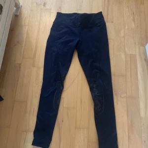 Mörkblå ridleggings från Svea - Snygga mörkblå ridbyxor från Svea Equestrian med tryck på benen och logga bak. De har hög midja och är gjorda i stretchigt material med 90% polyester och 10% elastan, vilket gör dem riktigt bekväma för ridning. Perfekta för dig som gillar att rida och vill ha stil på stallet.