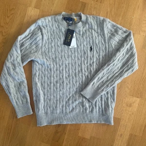 Grå Ralph lauren stickad tröja - Säljer denna stickade tröjan/cable knit med etikett. Säljs då den aldrig passade mig bra. Storlek S. (Har även en marinblå, se profil. Köper man båda så får man rabatt)