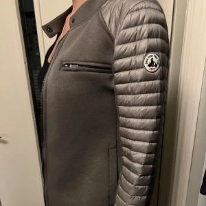 Grå cardigan jacka från JOTT - Snygg grå cardiganjacka från JOTT. Jackan har dragkedja framtill, bröstficka med dragkedja och diskret logga på ärmen. 