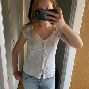 Vit spetsblus med knappar - Söt vit blus med korta ärmar och v-ringning. Blusen har spetsdetaljer över hela tyget och knäppning framtill med små vita knappar. Perfekt till jeans eller kjol för en fräsch look.