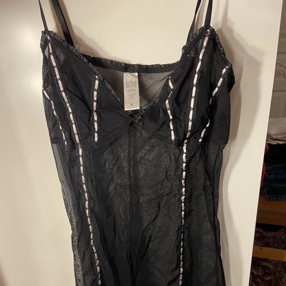 Ett svart nattlinne eller klänning i mesh med vita detaljer . Klänningar.