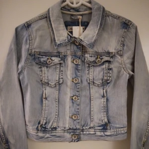 HELT NY & OANVÄND Snygg ljusblå jeansjacka, Strlk: 36 / SMALL. Inga defekter. - Helt NY & oanvänd ljusblå jeansjacka i vintage-stil. Storlek: 36/SMALL, passar eventuellt även någon med 32-34/XS. Lappar/tags sitter kvar sedan inköpet. Helt felfri.