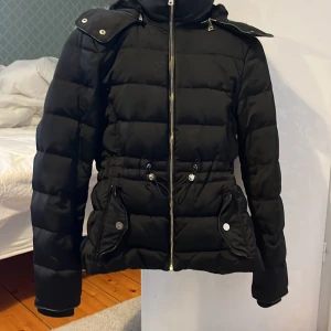 Zara jacka  - En svart vinterjacka med band så man kan dra åt i midjan. Jackan har även en dragkedja vid luvan så man kan ta bort den.  Den är fluffig inuti och i luvan. Den är använd ett fåtalgånger. Den är köpt på Zara Woman och är varm och gosig. Kund står för frakt