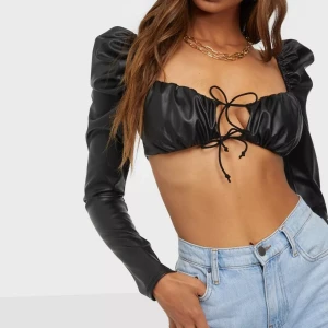 Svart croppad topp i PU - Svart croppad topp i PU-material från Nelly med resår på axlarna, långa ärmar och knytband framtill. Storlek M men skulle mer säga S/M. Helt oanvänd, enbart testad så den är som ny!   Nypris 349 kr. (De två första bilderna från Nellys hemsida)