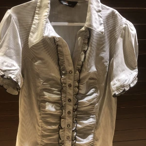 Satinskjorta - Kortärmad svart/vit randig satinskjorta. Skjortan har fina detaljer. I priset så är inte frakten inkluderad!!