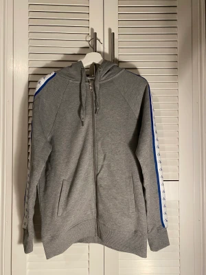 Grå - CalvinKlein ziphoodie - Här är en ziphoodie av Calvin Klein, Goodwin har mönster på sidorna av armarna som säger ”Ck” i blå tunn text tillsammans med en vit bakgrund. (Priset kan diskuteras)