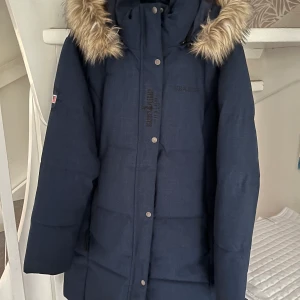 Vinterjacka Seaside i nyskick storlek 44 - Jättefin lång och varm vinterjacka köpt på Sporshopen. Använd fåtal ggr så i nyskick. Avtagbar huva med päls som också går att ta av själva huvan. Nypris 1200 kr säljes nu för halva priset.