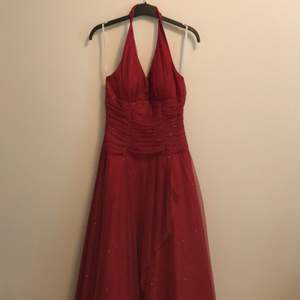 En lång röd balklänning. Klänningen är halterneck och glittrig. Med en fin knytning i ryggen. 