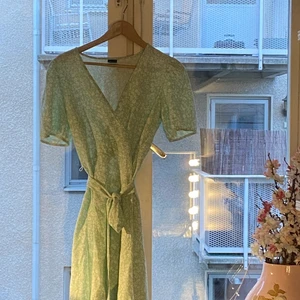 Grön blommig klänning  - Grön klänning med vita blommor! Fin till sommaren och har ett snöre till runt midjan 