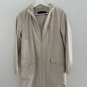Zara Regnjacka ljusbeige - En sparsamt använd regnjacka från Zara i galon. Stilrent innertyg i vitt - och beige randigt. Köpt för 700kr, säljes för 300. köparen står för frakt. 